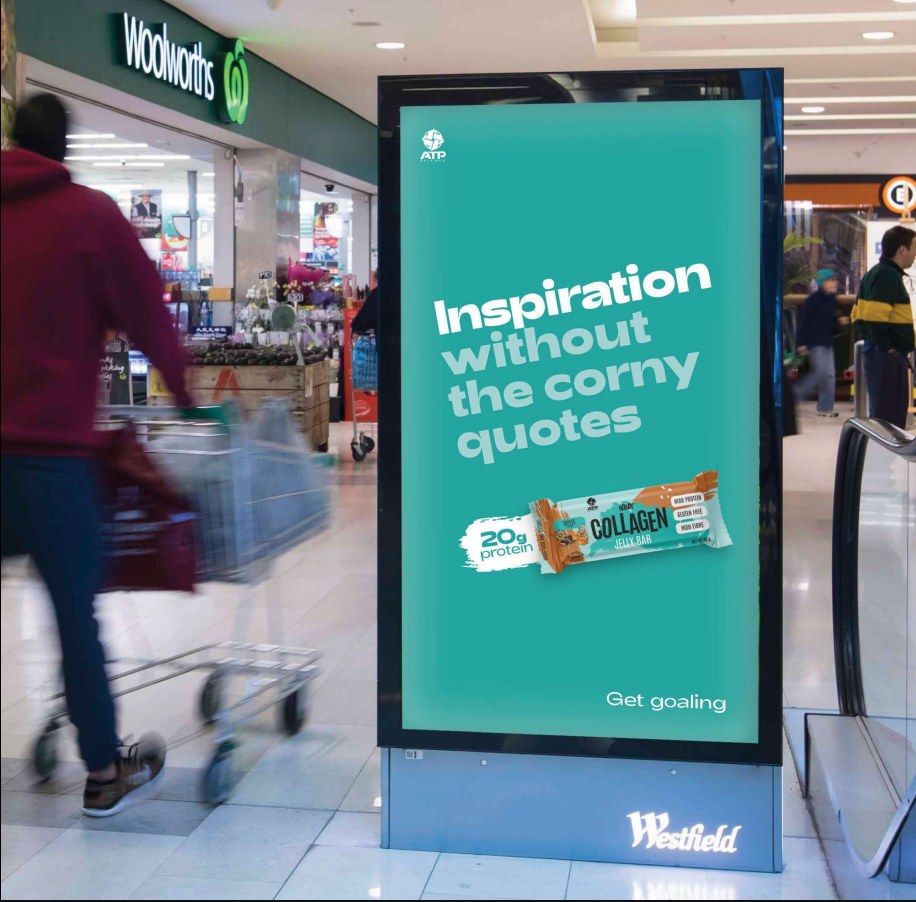 ATP Science collagen bar on a digital panel outside Woolworths in a Westfield centre, shopper pushing a trolley past
